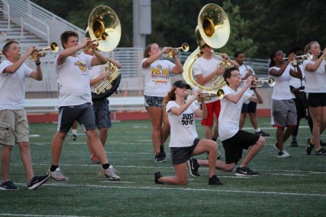 Ethan Wiedmier stands in a pose playing his trumpet while Grace Baer and Andrew Downs kneel while playing their trumpets during a halftime show.