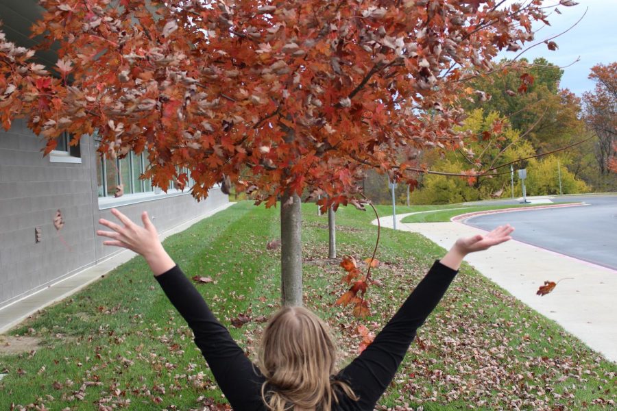 A student happily throws leaves in the air. (Allison Collier) 