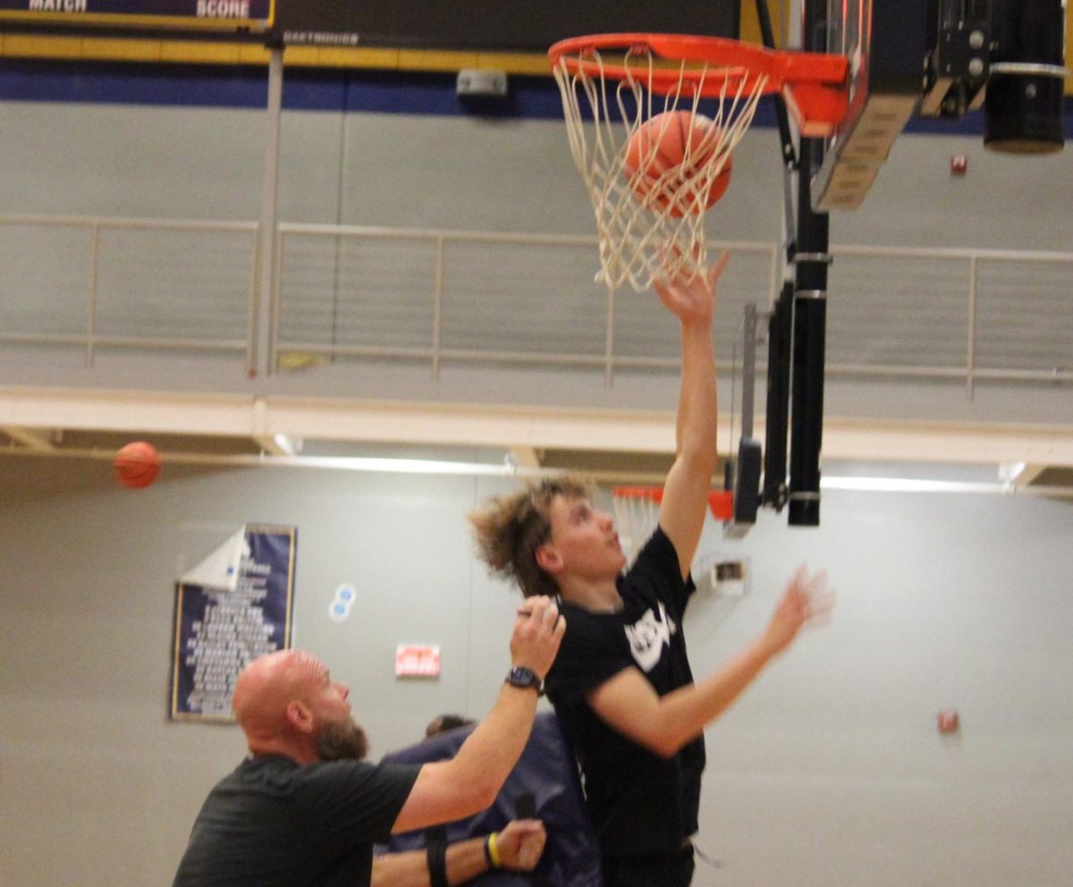 Senior Caden Lewis works on layups with contact with Assistant Coach Matt Hague at boys basketball practice on October 2 in the competition gym. 